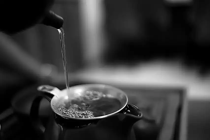 A delicate stream of hot water pouring into a traditional clay teapot
