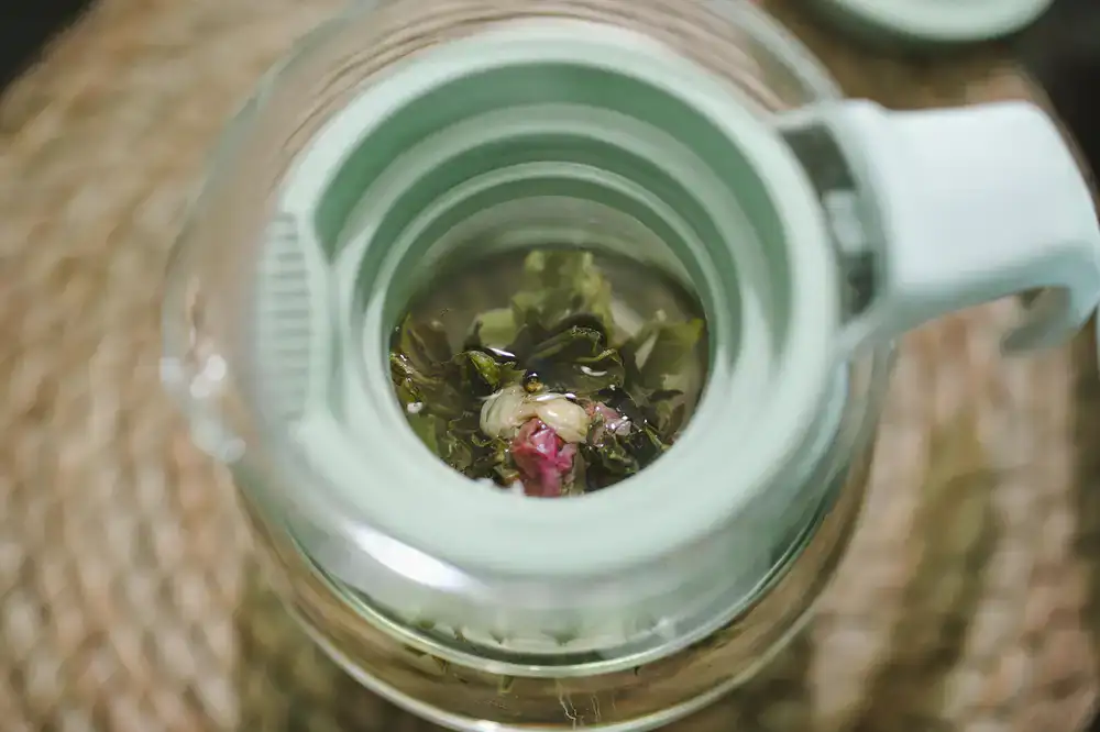 Clear glass teapot brewing pale green loose leaf tea